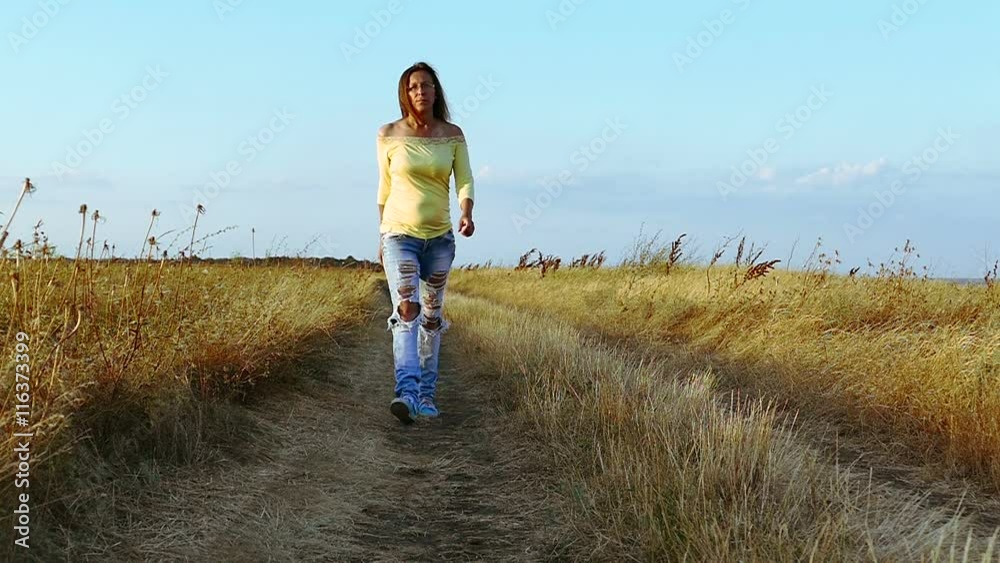 Slow motion. Serios woman in fashionable jeans goes on dirt road .Camera move
Slow motion. Serios woman in fashionable jeans goes on dirt road .Camera move