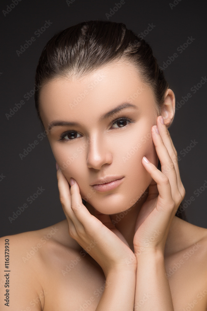Beauty Portrait. Beautiful Spa Woman Touching her Face. Perfect Fresh Skin. Beauty brunette Model. Youth and Skin Care Concept. Studio shot. Isolated on gray background