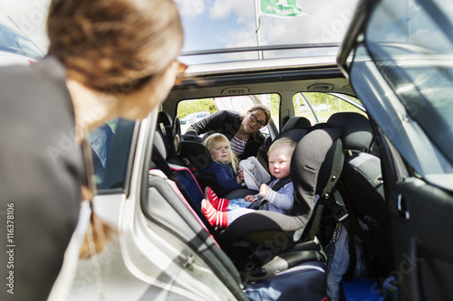 Women looking at children sitting in car photo