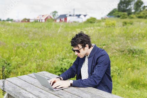 Man using laptop while sitting on grassy field photo