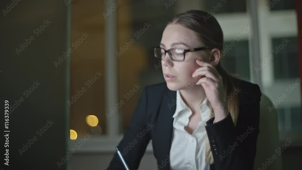Medium shot of tired sleepy businesswoman working on computer and making notes in dark office at night, yawning and massaging temples trying to concentrate, taken on Sony NEX700 + Odyssey 7Q Medium shot of tired sleepy businesswoman working on computer and making notes in dark office at night, yawning and massaging temples trying to concentrate, taken on Sony NEX700 + Odyssey 7Q