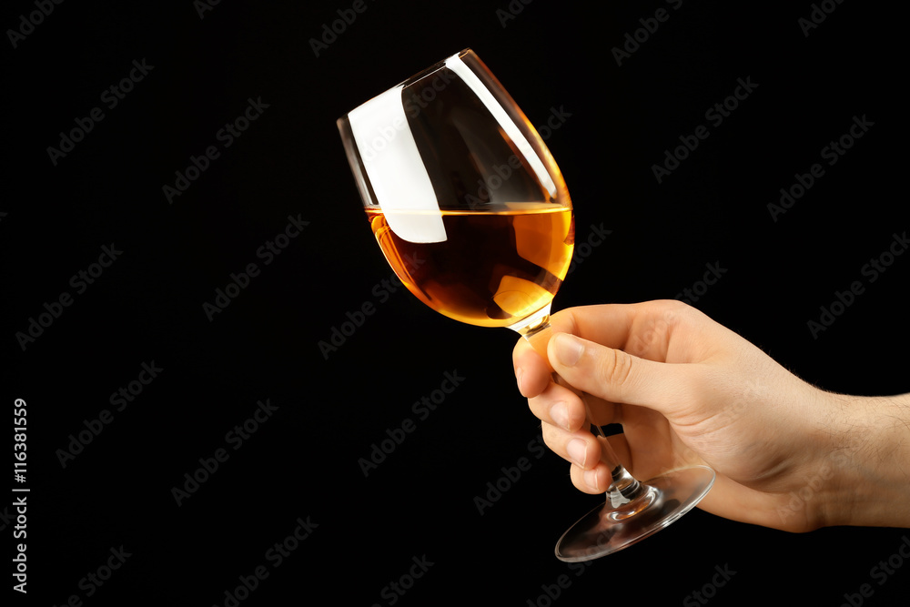 Male hand holding glass of wine on black background