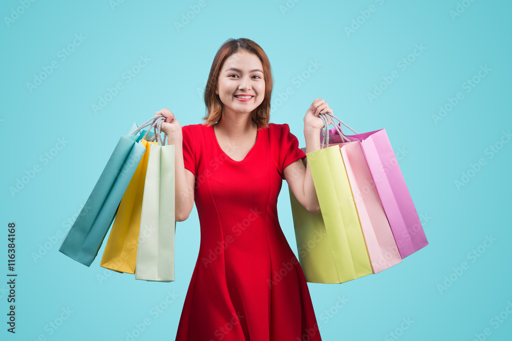 Beautiful young asian woman with colored shopping bags over blue