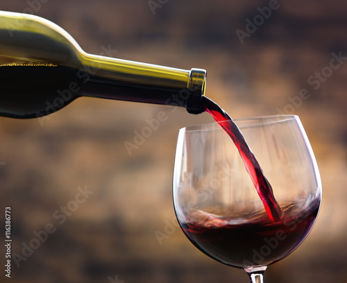 Red wine pouring in glass on brown background
