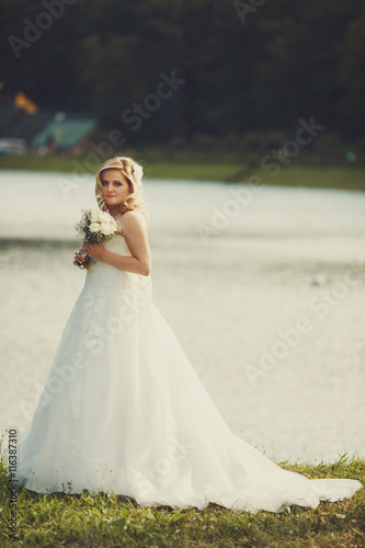 Pretty blonde bride stands on the lake shore in a shiny day