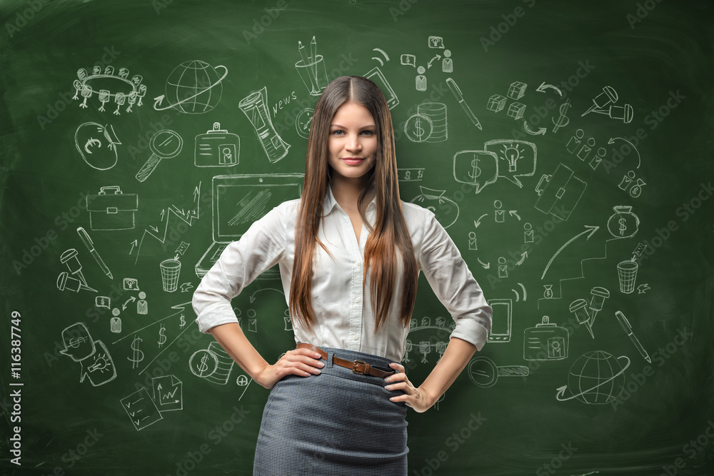 Young businesswoman looks directly at the camera and smiles on the background of the blackboard with chalk drawings