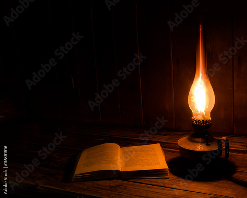 Old antique book opened with burning paraffin lamp near on the wooden table.