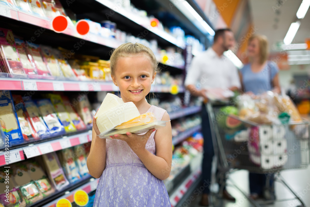 Girl holding cheese in hands in supermarket.