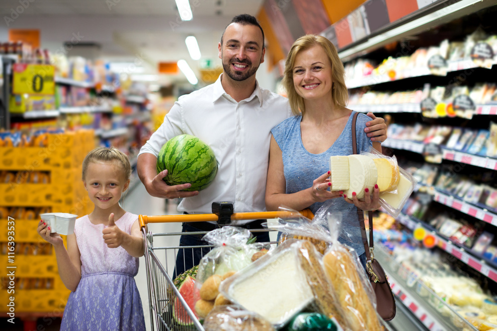 Happy family standing with full cart in supermarket