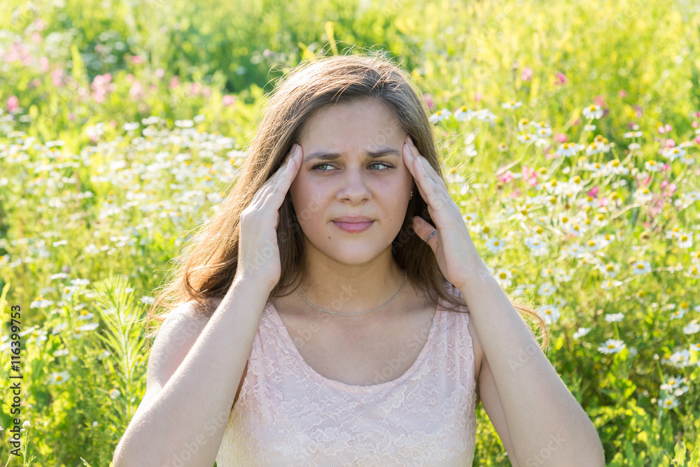 Teen girl with a headache on a blossoming meadow Teen girl with a headache on a blossoming meadow
