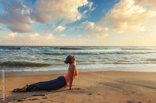 Woman practices yoga asana Urdhva Mukha Svanasana at the beach