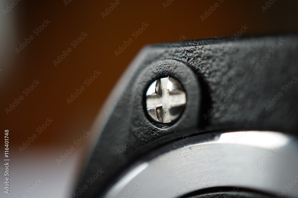 Macro detail of a cross-shaped metal screw connecting opposite parts of the plastic headphones Macro detail of a cross-shaped metal screw connecting opposite parts of the plastic headphones
