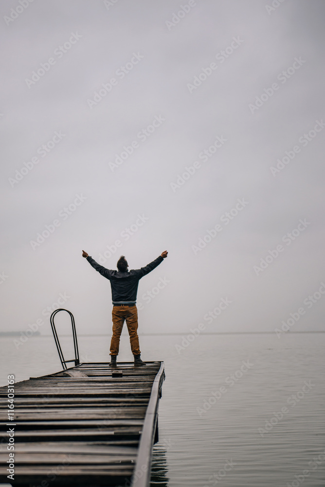 Fototapeta premium Man standing on a old wooden dock with raised hands