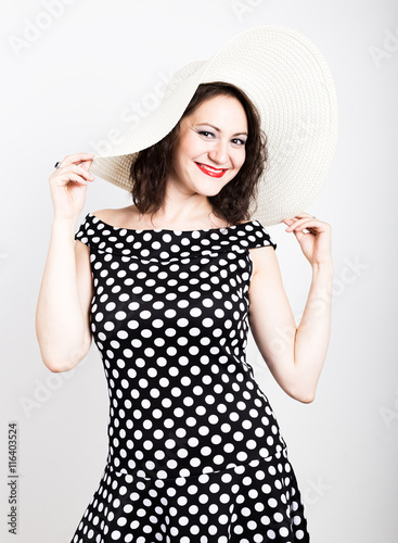 beautiful young brunette woman holding a broad-brimmed hat, she expression of different emotions. wears a dress with polka dots photo