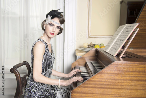 Pretty brunette in twenties theme sequinned dress sitting at harpsichord making eye contact with a nice smile photo