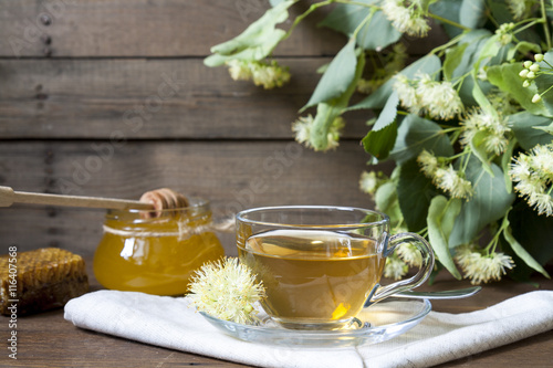 Linden tea in glass cup and jar with honey with linden flowers on a dark wooden background