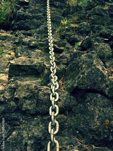 Detail of chain anchored in hard whinstone rock. Climbers path