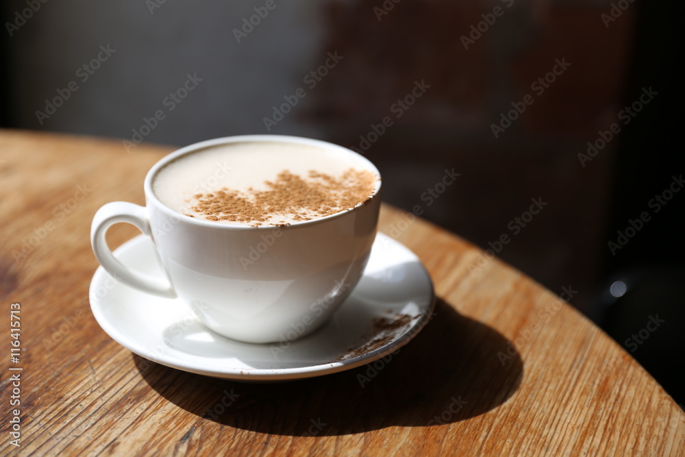 Obraz premium Cup of tasty latte is standing on the wooden textured table with the brick wall background. Latte is in the white big cup.