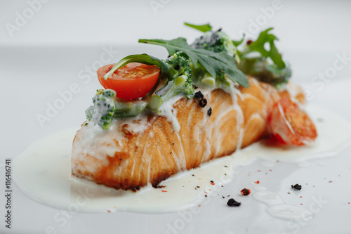 red fish in white sauce with tomatoes, broccoli and greens on white background
