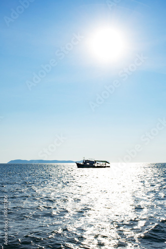 silhouette fishing boat in the ocean with sun and blue sky © mckaphoto