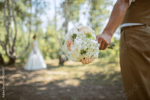 man's hand holding a bridal bouquet, the background blurred silhouette of a bride