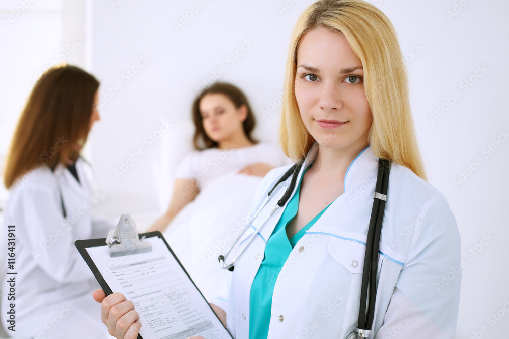 Young beautiful female doctor smiling on the background with patient and his physician in hospital. High level and quality medical service concept. Young beautiful female doctor smiling on the background with patient and his physician in hospital. High level and quality medical service concept.
