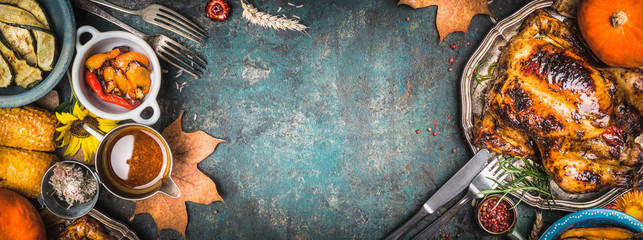 Delicious roasted whole chicken or turkey on plate with cutlery and sauce , harvest grilled vegetables on dark rustic background, top view, banner, frame. Thanksgiving Day food