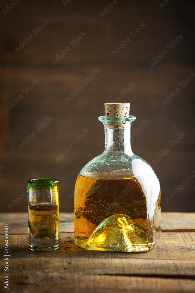 Gold tequila in glass on wood table. Selective Focus. Blurred background.