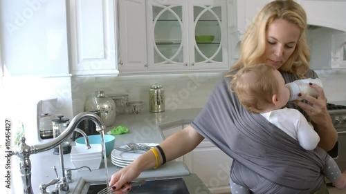 Busy Mother With Baby In Sling At Home