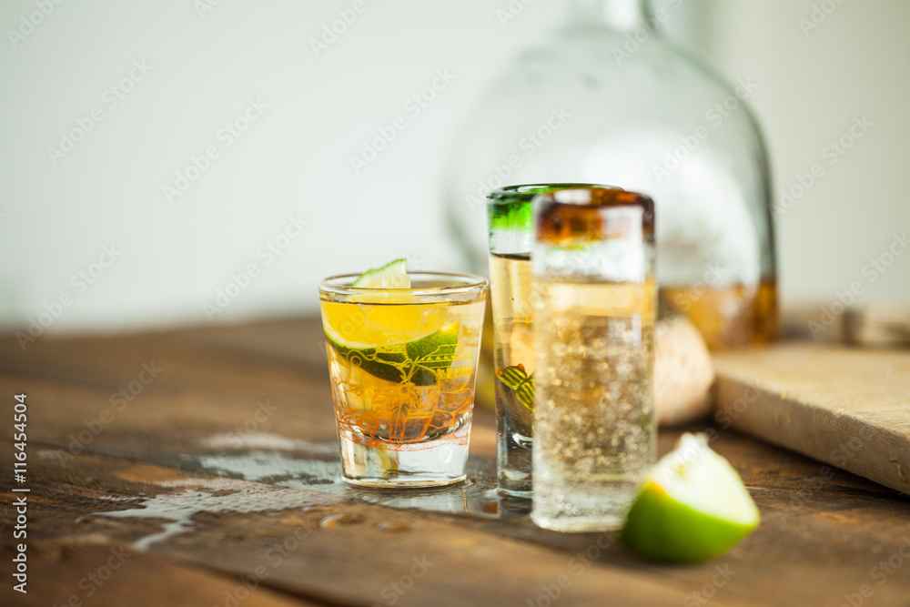 Shot glass of tequila on wood table. Selective focus. Blurred background. Shot glass of tequila on wood table. Selective focus. Blurred background.