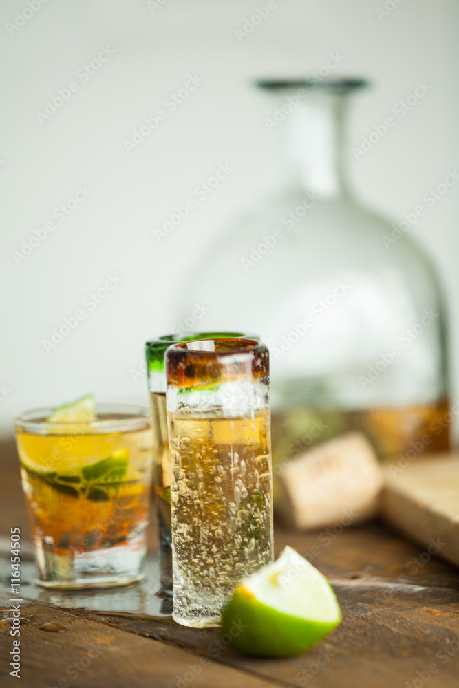 Shot glass of tequila on wood table. Selective focus. Blurred background. Shot glass of tequila on wood table. Selective focus. Blurred background.