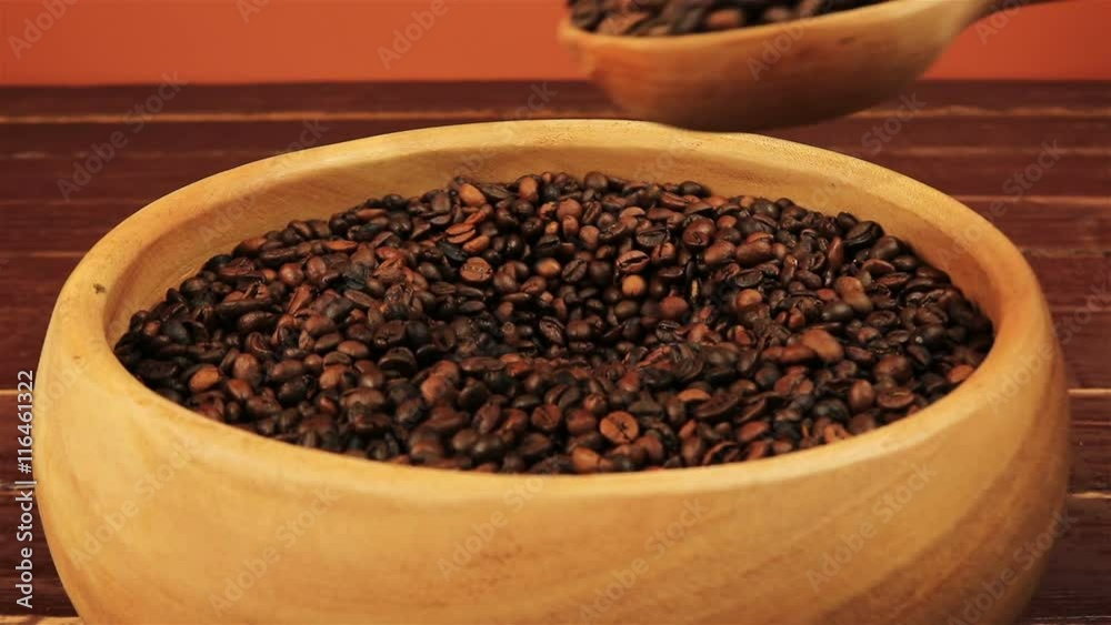 Taking coffee beans by using wooden spoon in wooden bowl on brown wooden table Taking coffee beans by using wooden spoon in wooden bowl on brown wooden table