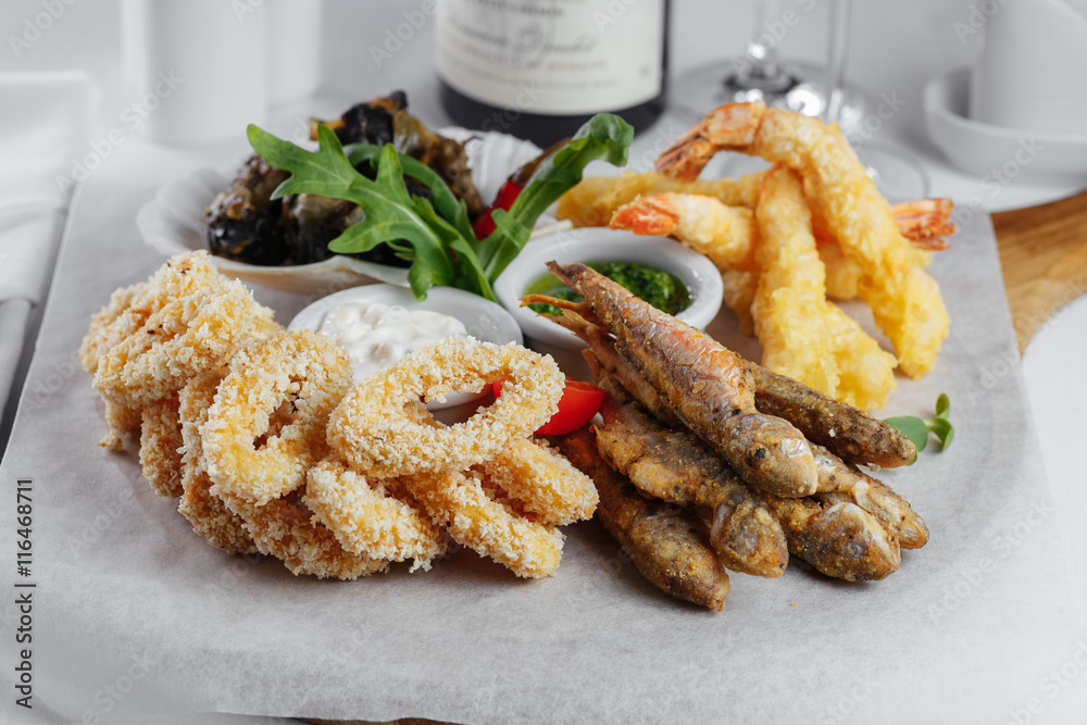 fried fish with sauce and greens with squid rings, mussels and shrimp on a white paper fried fish with sauce and greens with squid rings, mussels and shrimp on a white paper