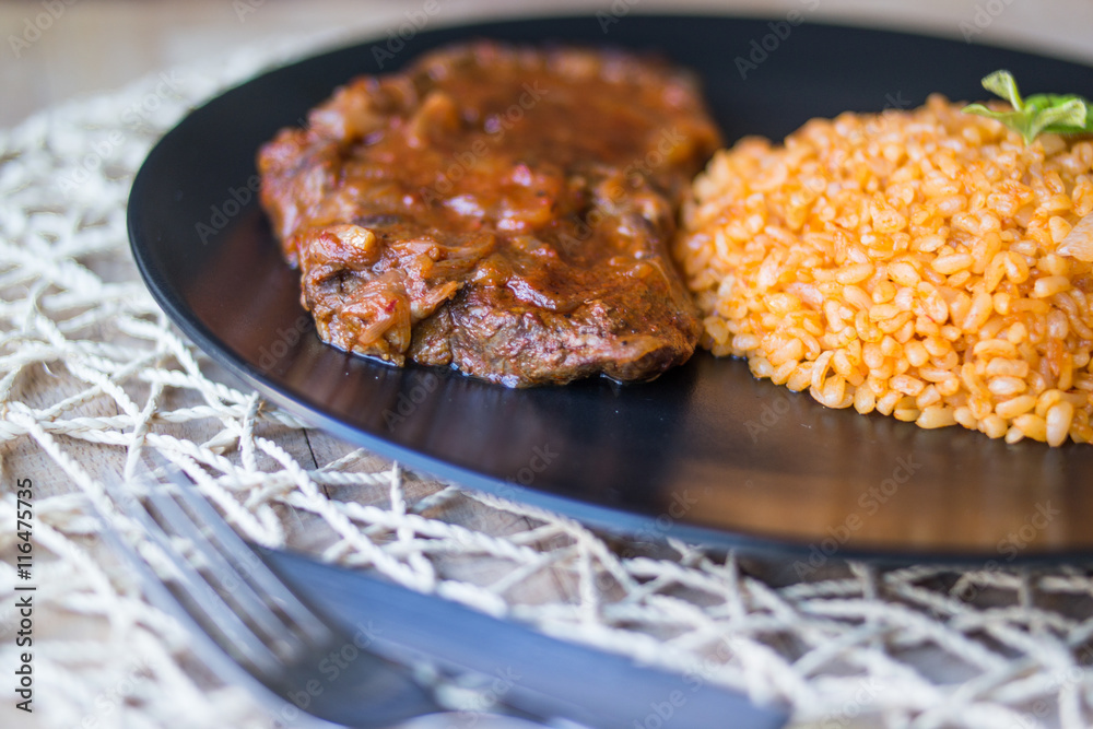 Steak with tomato sauce and bulgur rice in a black plate
