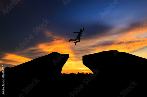 Man jump through the gap between hill.man jumping over cliff on sunset background Business concept idea