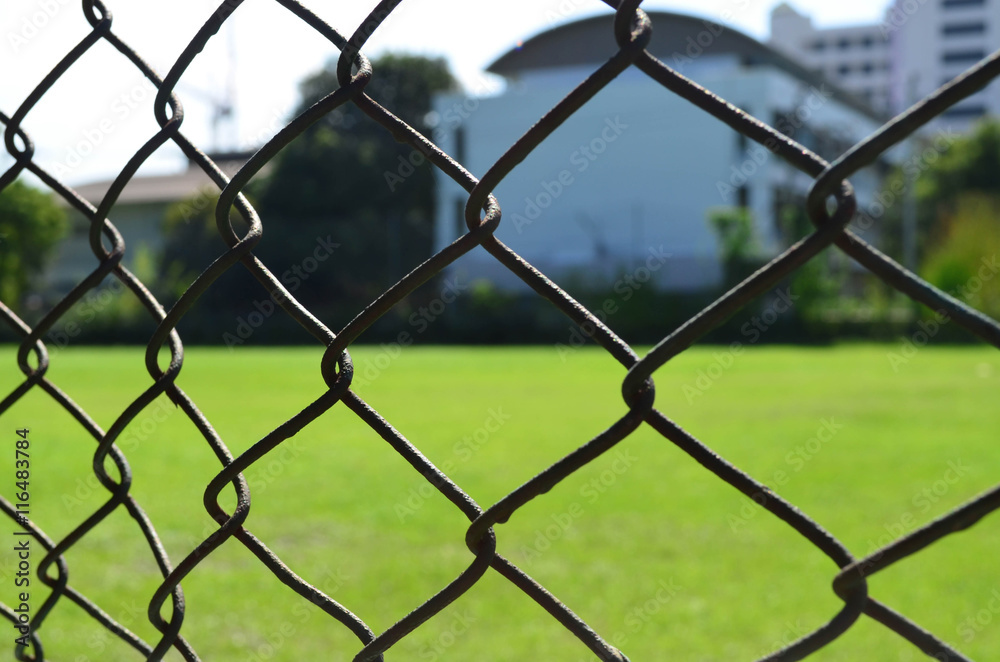 Security wire mesh fence with field and building background Security wire mesh fence with field and building background