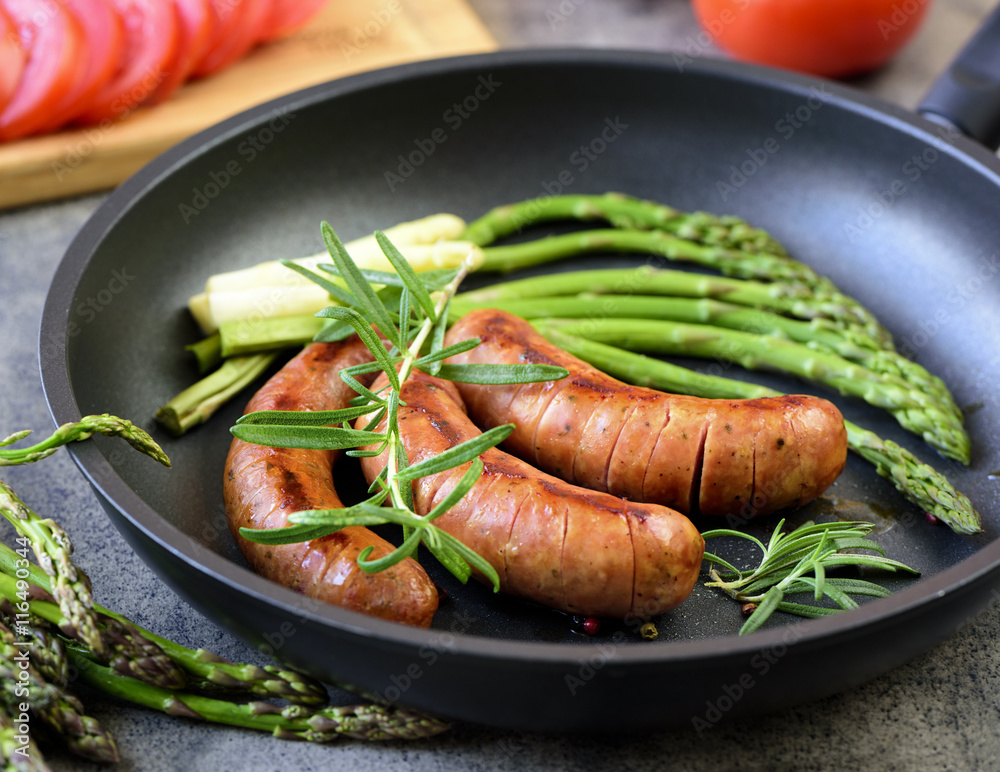 sausages with asparagus, tomatoes and rosemary on a pan sausages with asparagus, tomatoes and rosemary on a pan