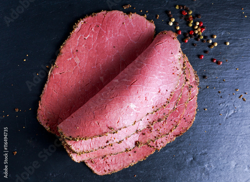 Peppered roast beef pastrami slices on paper with grains of coloured pepper.