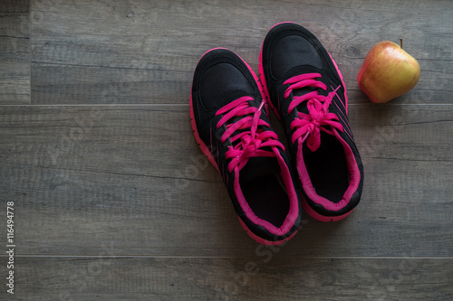 Pink sport shoes with apple on wooden background