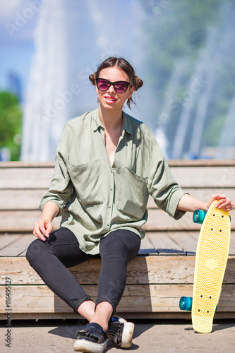 Young girl having fun with skateboard in the park. Lifestyle portrait of young positive woman having fun and enjoy warm weather.