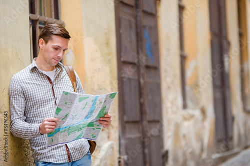 Man tourist with a city map and backpack in Europe street. Caucasian boy looking with map of European city in search of attractions.