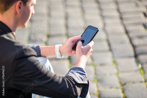 Closeup of male hands is holding cellphone outdoors on the street. Man using mobile smartphone.