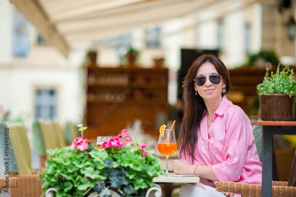 Portrait of young beautiful woman sitting in a cafe outdoor drinking tasty cocktail. Happy tourist enjoy european holidays at openair restaraunt Portrait of young beautiful woman sitting in a cafe outdoor drinking tasty cocktail. Happy tourist enjoy european holidays at openair restaraunt