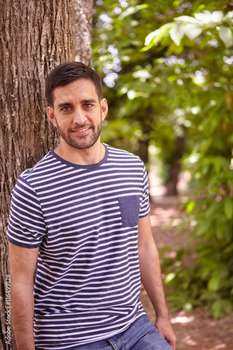 Smiling young man leaning against tree