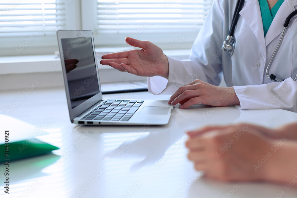 Doctor pointing into laptop computer and discussing something with her patient. Close-up.