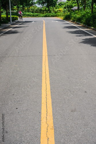 blacktop with double yellow lines divider under sunshine, an unrecognizable lady riding a bicycle coming