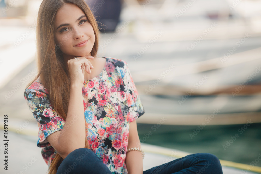 Closeup portrait of young beautiful woman with grey eyes,brunette with long straight hair,light makeup and cute smile,dressed in a colorful blouse,posing in the summer outdoors