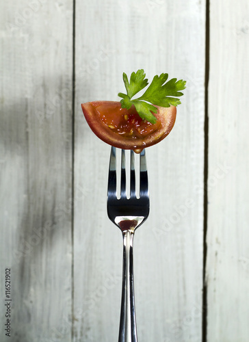 Ripe tomato with parsley on a fork. Background