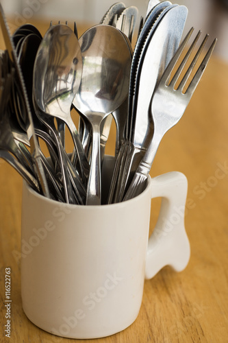 Kitchenware , spoons knifes and forks in white mug on wooden table