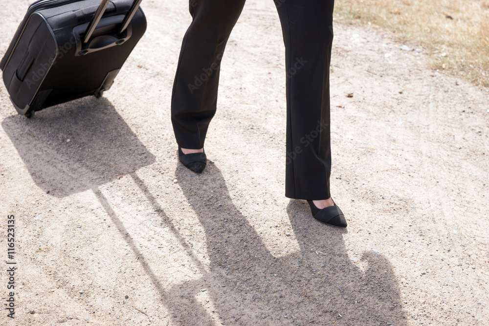 Woman walking on the dirt road with hand luggage suitcase